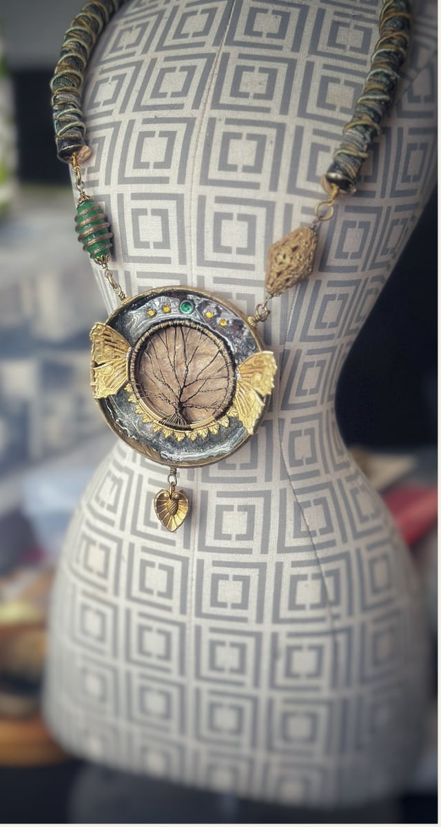 A one-of-a-kind mixed-media pendant necklace in brass and resin, shown on a studio dress form.